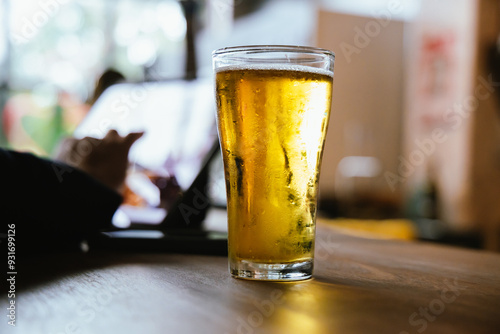 A man pours frothy beer into a glass at a lively pub. Friends gather around the bar, enjoying drinks and celebrating, with a warm, golden glow highlighting the joyful, friendly atmosphere.