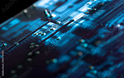 Close-up of an illuminated blue electronic circuit board with many electrical components, isolated on black background, selective focus