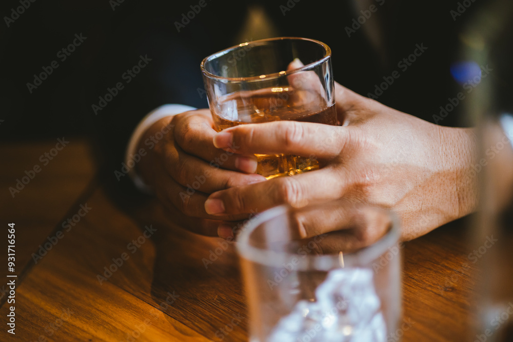 A stylish man holds a glass of whiskey in a fancy pub amidst a crowd of celebrants. The warm and elegant atmosphere accentuates the rich amber-colored liquid.