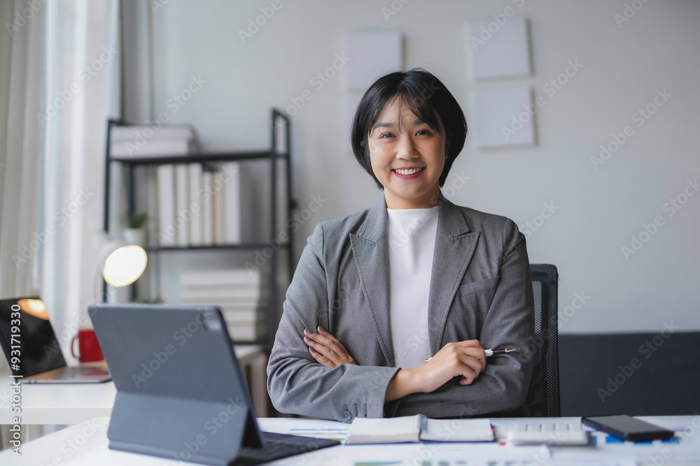 Asian businesswoman is smiling while sitting at her desk with her arms crossed in her office Asian businesswoman is smiling while sitting at her desk with her arms crossed in her office