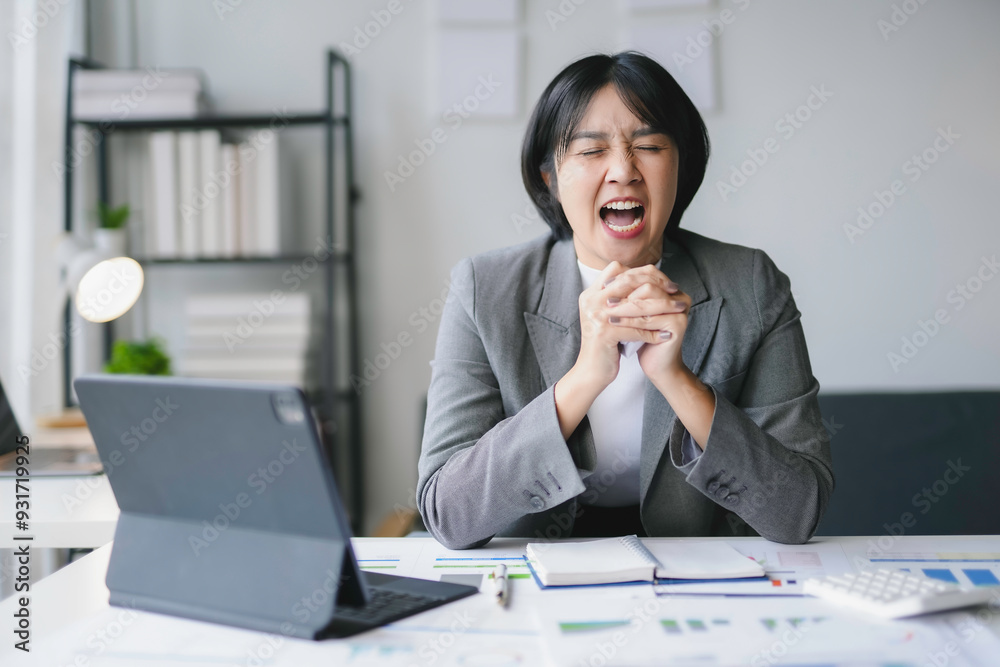 Young businesswoman is sitting at her desk with her eyes closed and screaming, appearing to be under a lot of pressure Young businesswoman is sitting at her desk with her eyes closed and screaming, appearing to be under a lot of pressure