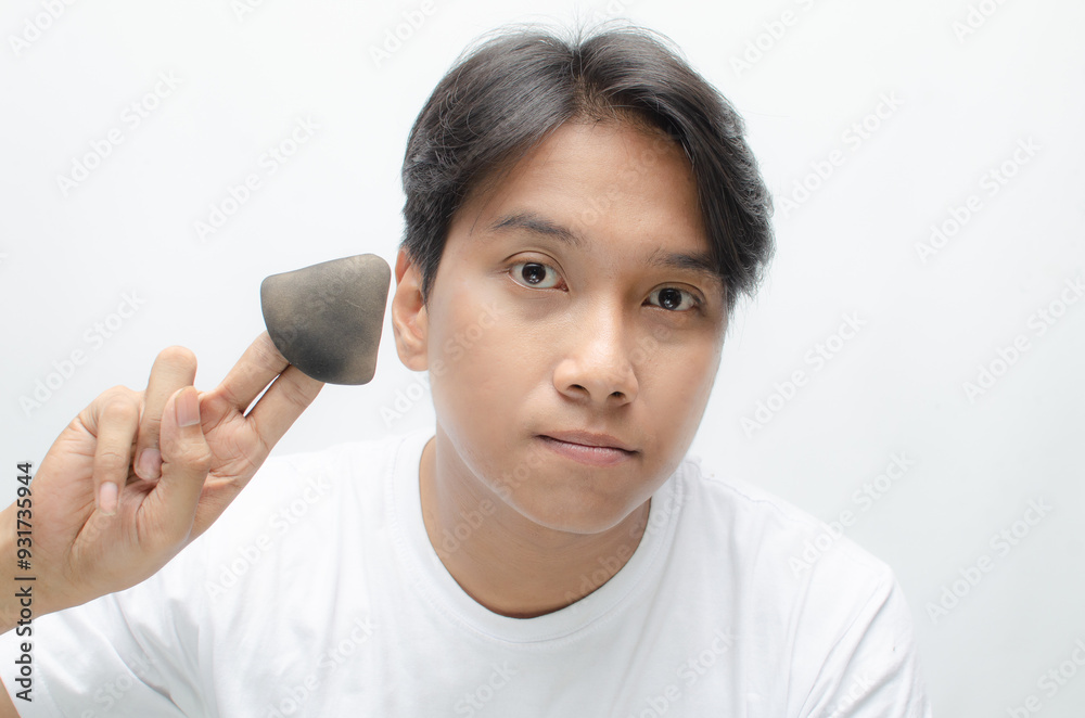 close-up young attractive asian man applying powder puff and cushion for facial makeup. young asian man in white tshirt doing makeup. close-up young attractive asian man applying powder puff and cushion for facial makeup. young asian man in white tshirt doing makeup.