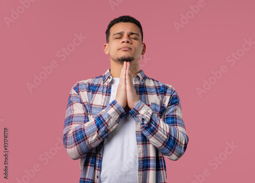 Young multiracial man praying with crossed fingers on pink. Guy begs someone