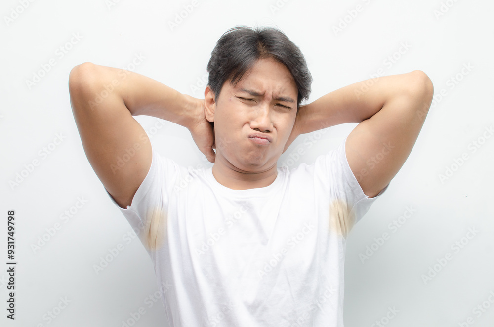 asian man feels bad after smelling his armpit with yellow stain on his white tshirt. young asian man smells his bad odor armpit with disgusted face. asian man feels bad after smelling his armpit with yellow stain on his white tshirt. young asian man smells his bad odor armpit with disgusted face.