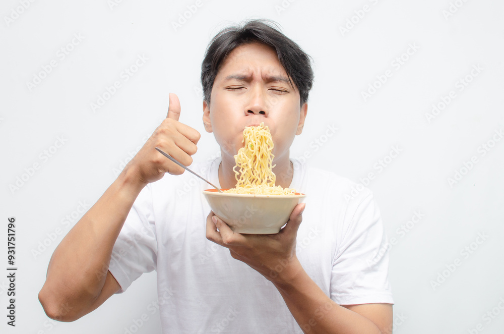 young asian man eats noodles. ecstatic young asian man with mouth full of noodles. young man in white tshirt enjoying noodles. young asian man eats noodles. ecstatic young asian man with mouth full of noodles. young man in white tshirt enjoying noodles.
