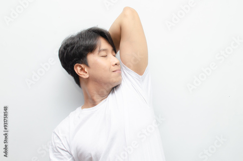 A young Asian man in white tshirt smells the freshness of his odor from armpit. Man enjoys his freshness and cleanliness. man smelling his armpit