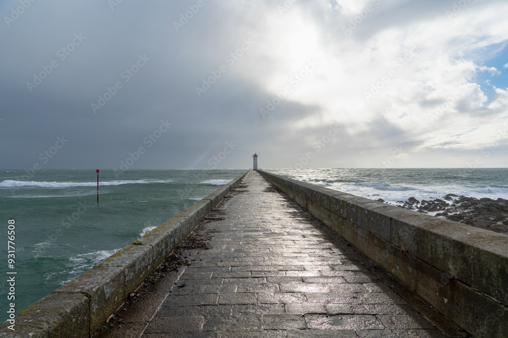 Le phare du Raoulic se reflète partiellement sur le sol mouillé du môle, où les reflets des nuages et du soleil dansent en Bretagne.