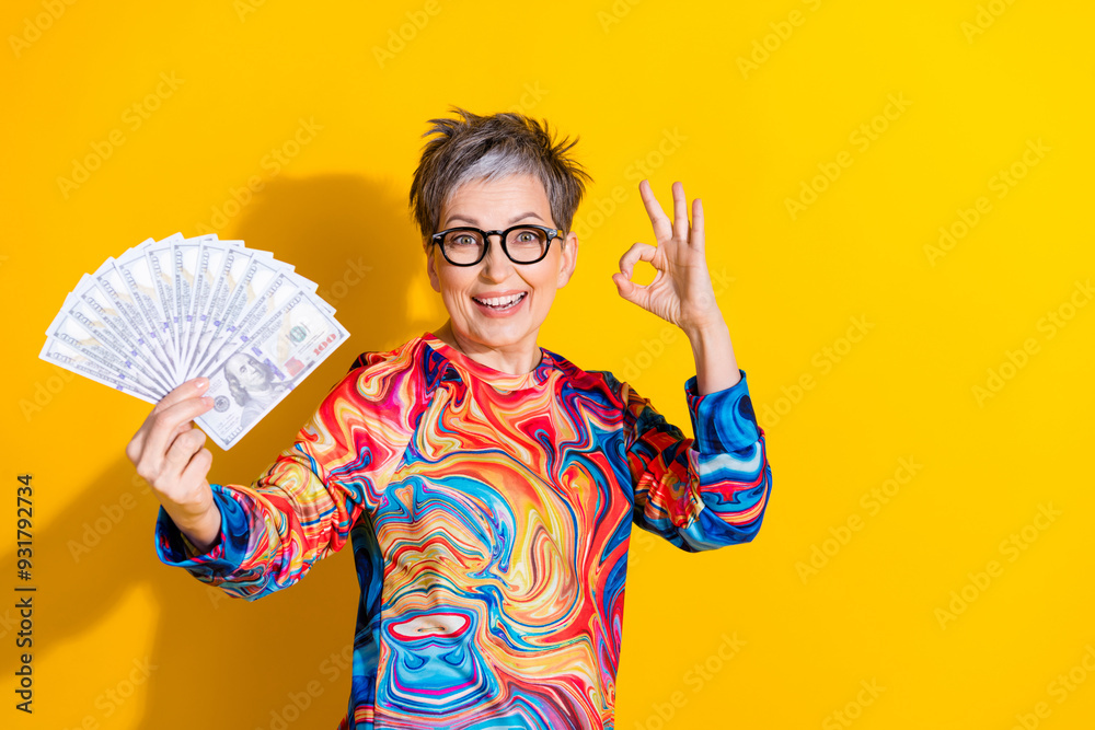 Photo of nice aged woman okey symbol hold money wear pullover isolated on yellow color background Photo of nice aged woman okey symbol hold money wear pullover isolated on yellow color background