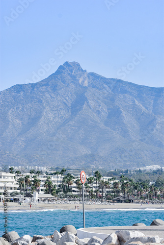 Vista panorámica de la playa de Marbella, con el mar cristalino en primer plano y las majestuosas montañas al fondo. Esta imagen captura la impresionante combinación de playa y paisaje montañoso.