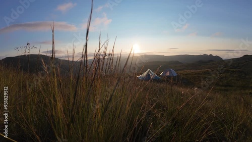 Slow motion grass blowing in wind with 2 tents at sunrise