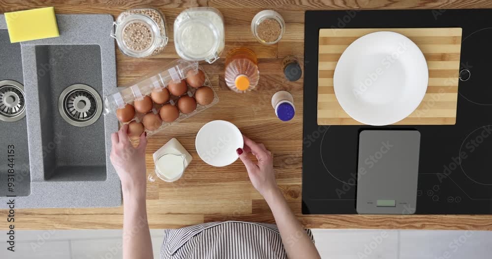 Woman cook puts eggs in bowl with milk, top view