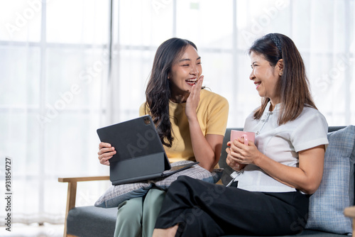 Two women sitting on a couch, one holding a tablet and the other holding a cup