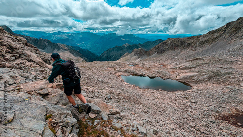 With the peaks of the Eristes in the background and the ibones of Bagüeñola reflecting the sky, a mountaineer enjoys a day in the Aragonese Pyrenees, Huesca, surrounded by lush alpine vegetation. photo