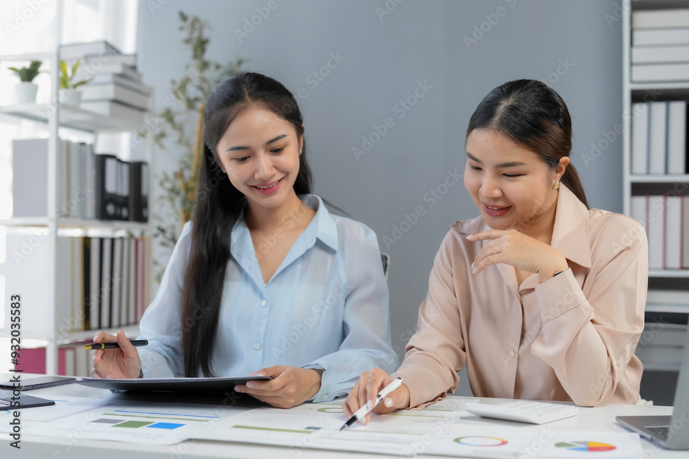 Two young businesswomen smiling while working together on financial data analysis in their bright modern office Two young businesswomen smiling while working together on financial data analysis in their bright modern office