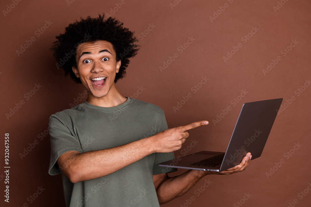 Photo of young guy in gray t shirt remote working remote using laptop pointing finger at display isolated on brown color background Photo of young guy in gray t shirt remote working remote using laptop pointing finger at display isolated on brown color background