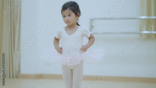 Adorable shy little ballerina is practicing in a dance studio classroom. Happy kid student in white tutu dances, learning a lesson of balancing on a pointe shoes in ballet class. Hobby Activity