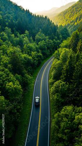 A car is driving down a road surrounded by trees. The road is wide and the trees are lush and green. The car is a black sedan and it is driving down the road in the middle of the forest