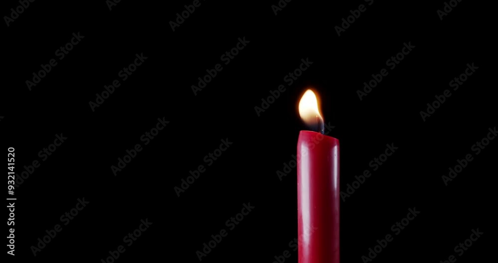 A single red candle burning. Isolated candle burning with dark background. Red paraffin candle with yellow shades burns on a black background. Background or illustration of remembrance or celebration. A single red candle burning. Isolated candle burning with dark background. Red paraffin candle with yellow shades burns on a black background. Background or illustration of remembrance or celebration.