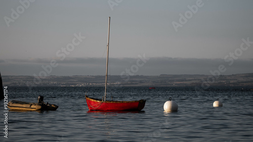 Small red sailing boat at the entrance to a marina