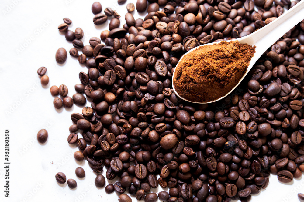 Overhead view of a spoonful of coffee powder on a stack of roasted coffee beans Overhead view of a spoonful of coffee powder on a stack of roasted coffee beans