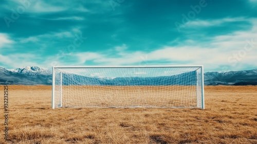 A soccer goal stands in a grassy field with mountains under a blue sky