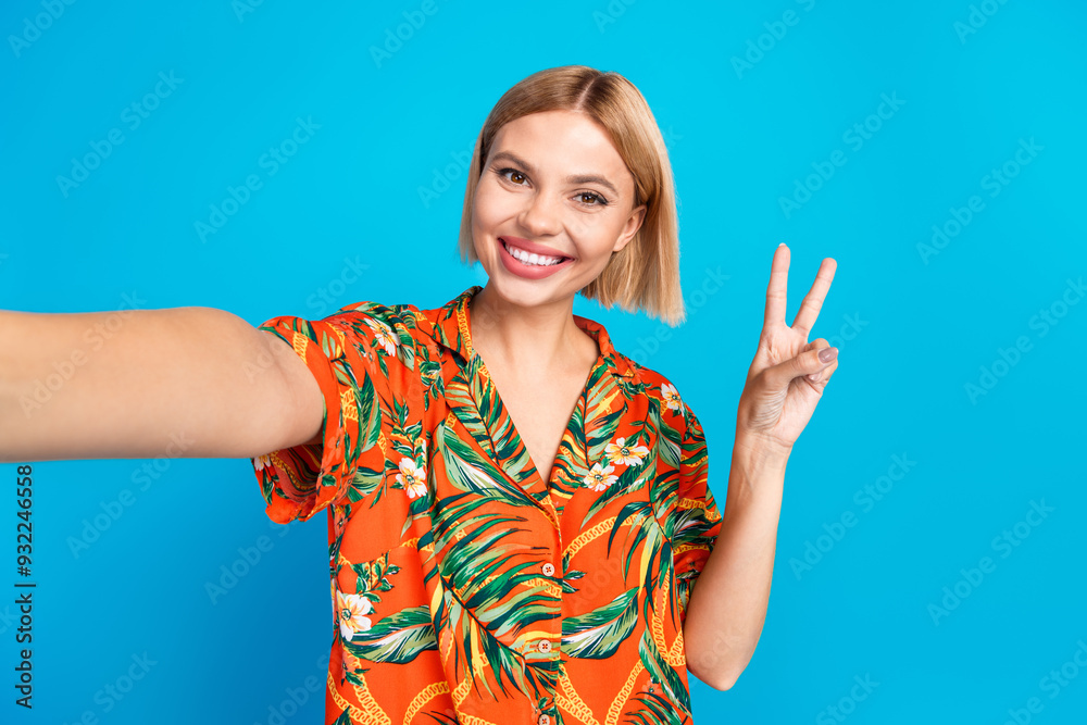 Photo of cheerful adorable girl wear stylish orange print clothes recording video v-sign isolated on blue color background Photo of cheerful adorable girl wear stylish orange print clothes recording video v-sign isolated on blue color background