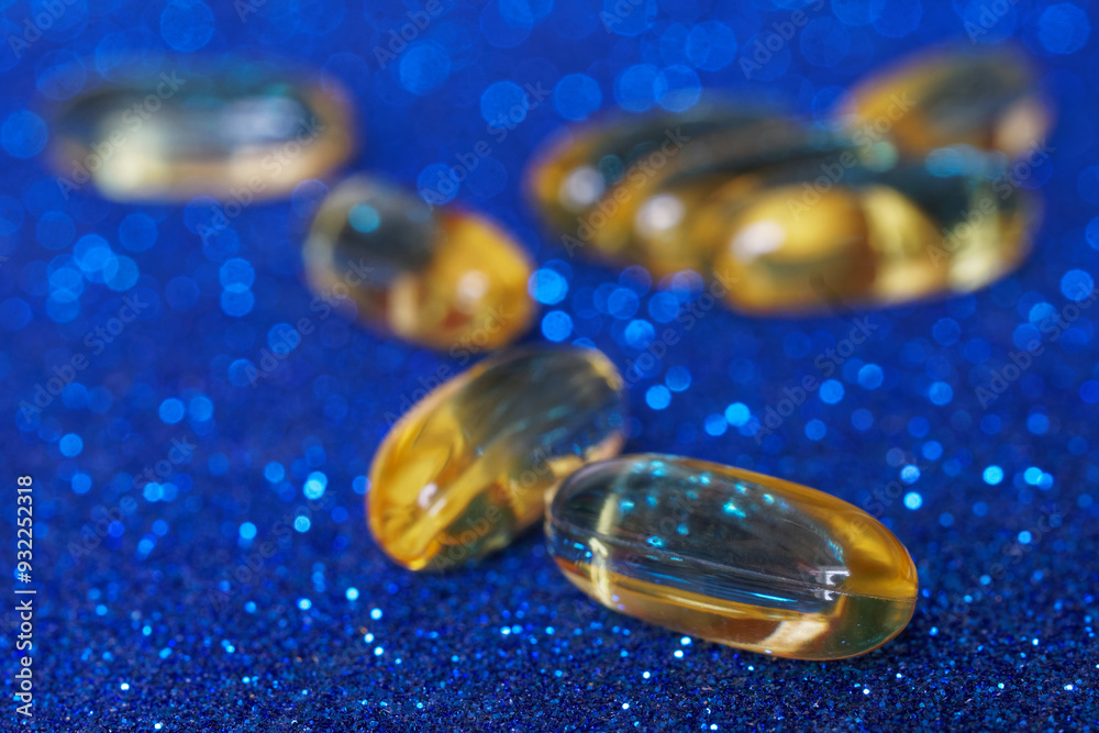 Golden capsules with edible fish oil lie on a blue sparkling surface. Photo. Macro. Selective focus. Shallow depth of field. Golden capsules with edible fish oil lie on a blue sparkling surface. Photo. Macro. Selective focus. Shallow depth of field.