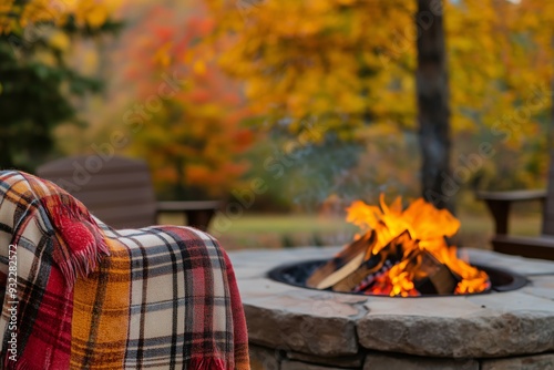 Fototapeta Naklejka Na Ścianę i Meble -  A cozy outdoor setting with a warm fire pit and a plaid blanket next to it. Warm fire pit for a relaxing fall feel.