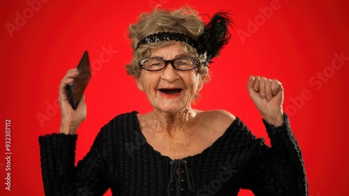 Portrait of toothless elderly senior old woman with wrinkled skin looking at phone having great happy success winner isolated on red background. People emotions concept.
