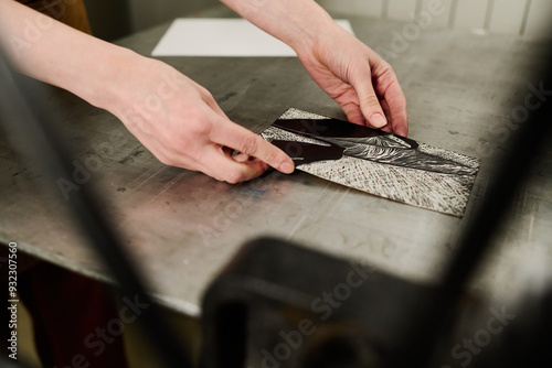 Hands of young unrecognizable female worker of typography house putting handmade artwork on steel tray of printing equipment photo