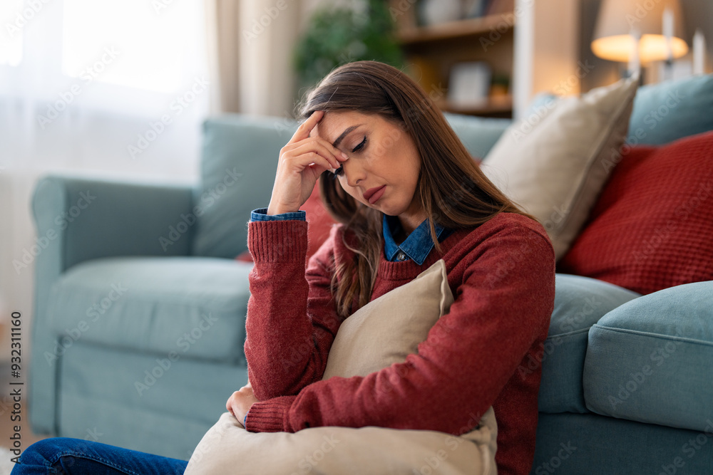 A pensive Caucasian woman, dressed in casual sweater and jeans, seeks comfort gripping a pillow in a cozy living room setting, reflecting a moment of unease. A pensive Caucasian woman, dressed in casual sweater and jeans, seeks comfort gripping a pillow in a cozy living room setting, reflecting a moment of unease.