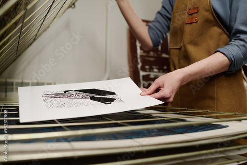 Cropped shot of young unrecognizable female worker of printing center putting paper with artwork sketch on tier of machine photo