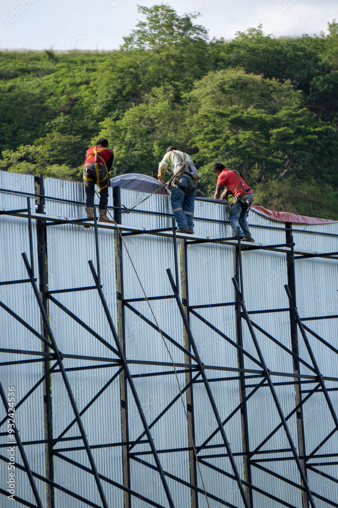 Three workers secure tarp to the back of an external billboard structure Three workers secure tarp to the back of an external billboard structure