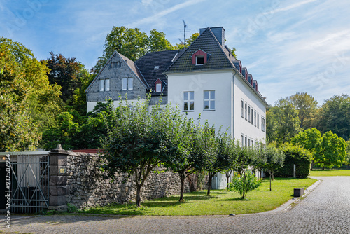 Beautiful white house surrounded by trees and greenery, situated inside the grounds of Klosterruine Heisterbach, with a peaceful sky above. photo