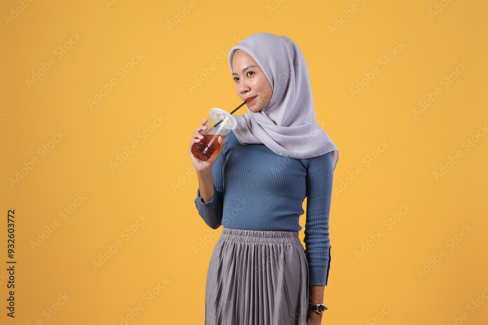portrait of happy asian indonesian muslim woman drinking cold ice tea in plastic cup on isolated yellow background portrait of happy asian indonesian muslim woman drinking cold ice tea in plastic cup on isolated yellow background