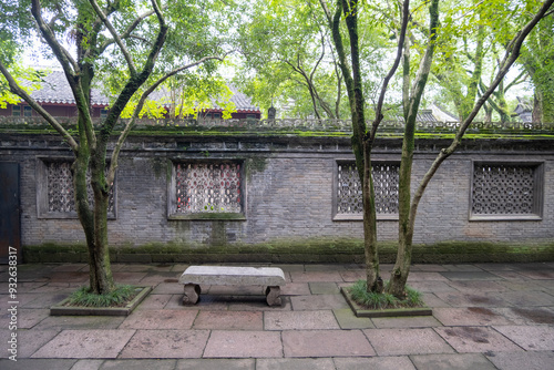 A traditional Chinese courtyard with a gray stone wall featuring several windows with intricate latticework, and a weathered stone bench. A peaceful place to rest in a historic garden. Tianyige Ningbo photo