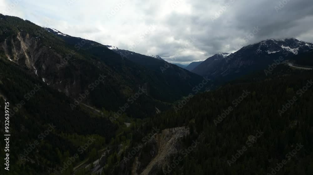Beautiful aerial view of a mountain valley with a dense forest. Clouds cast shadows on the mountain sides. Dramatic sky. British Columbia, Canada. Beautiful aerial view of a mountain valley with a dense forest. Clouds cast shadows on the mountain sides. Dramatic sky. British Columbia, Canada.