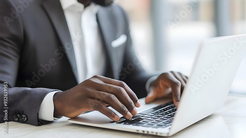 A person in a suit typing on a laptop in a modern workspace.