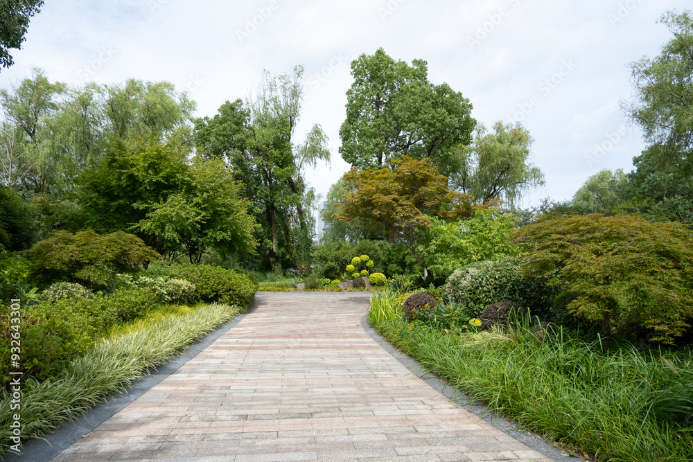 Background texture of a paved pathway lined with lush greenery, various plants and trees in a well-landscaped urban park. A walkway in a public green space. Copy space for design Background texture of a paved pathway lined with lush greenery, various plants and trees in a well-landscaped urban park. A walkway in a public green space. Copy space for design