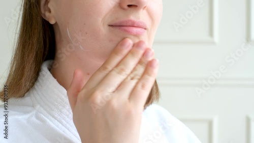 Portrait of a young woman applying moisturizer to her face close-up. photo