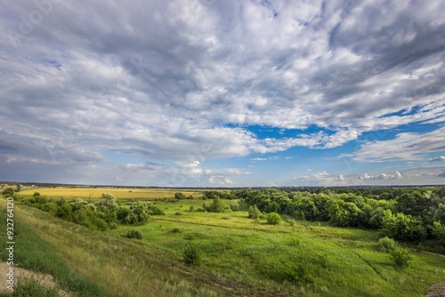 A lush green meadow stretches out beneath a sky filled with dramatic clouds, as gentle hills rise in the distance inviting exploration and tranquility.