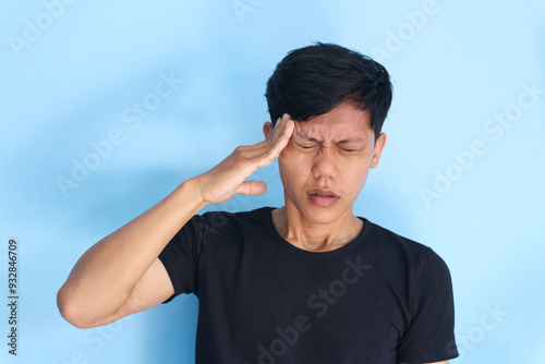 young asian man showing pain expression while touching head with his hand