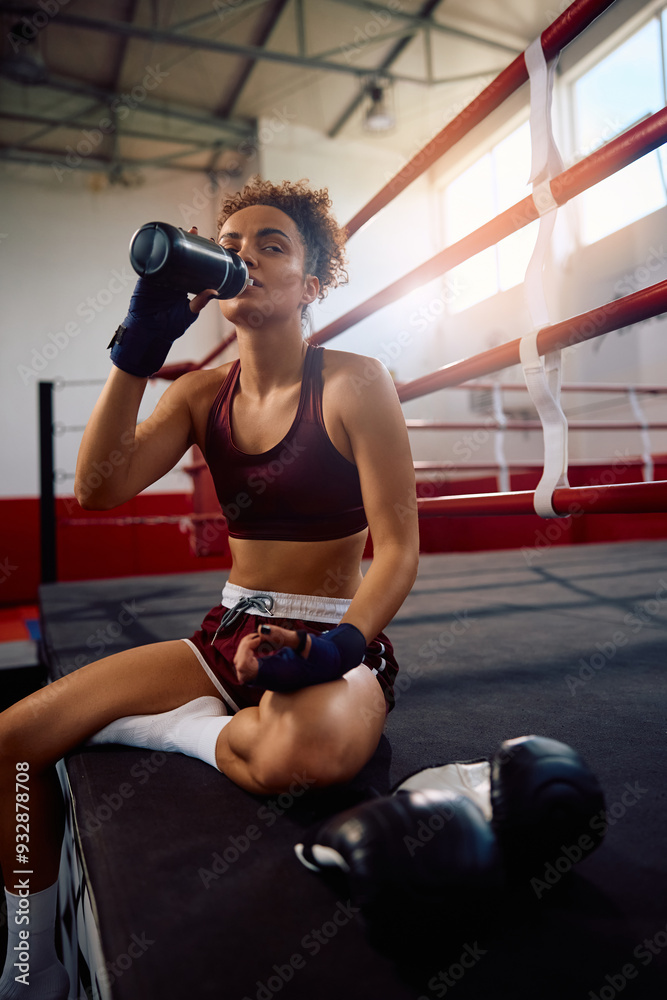 Naklejka premium Female fighter drinking water from bottle while resting after boxing training.
