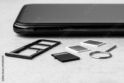 smartphone with open slots for micro SD and nano SIM cards, two nano SIM cards and metal key on grey background black white photo