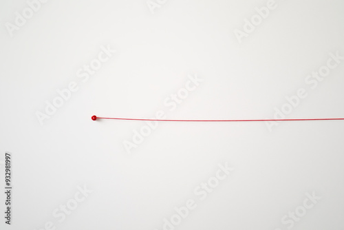 A red string is stretched out on a white wall