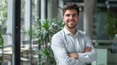 Smiling handsome businessman with crossed arms in modern office,young man exuding confidence, business success concept.