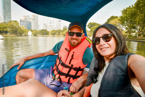 Happy young caucasian couple take selfie look at camera enjoy sport activity on pedal boat in famous public Lumphini park in summer. Bangkok relaxation leisure activities photo