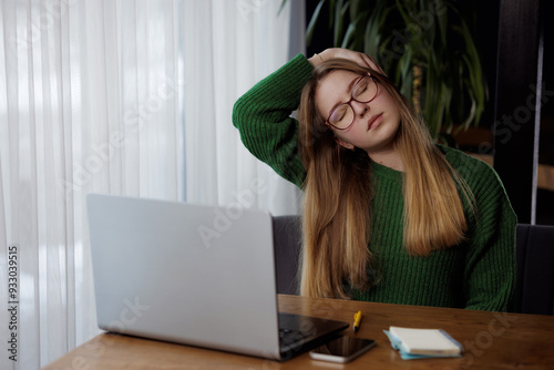 Young woman doing neck stretch while working on computer in home office