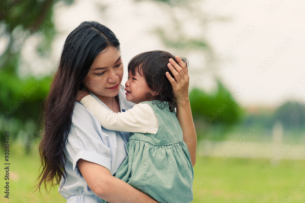 mother holding and comforting her crying toddler baby girl on grass field in park mother holding and comforting her crying toddler baby girl on grass field in park