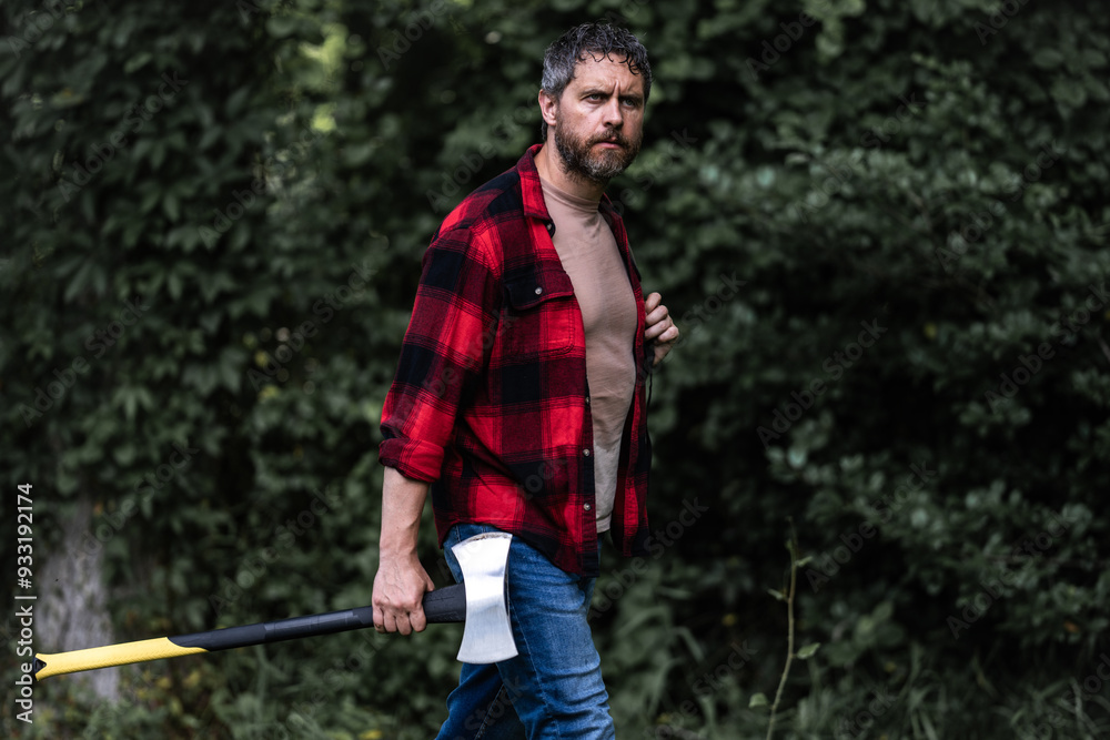 Fototapeta premium Lumberjack in shirt with heavy axe. Strong man work in forest. Lumber jack men in forest with axe. Lumberjack carries axe. Deforestation. Handsome man with axe. Lumberjack in the woods with an ax.